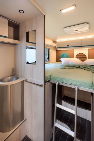 Elegantly arranged bedroom in a Nomad Camper located in Albania, featuring a comfy double bed with teal accents, accessible by a sleek ladder, showcasing smart use of space.