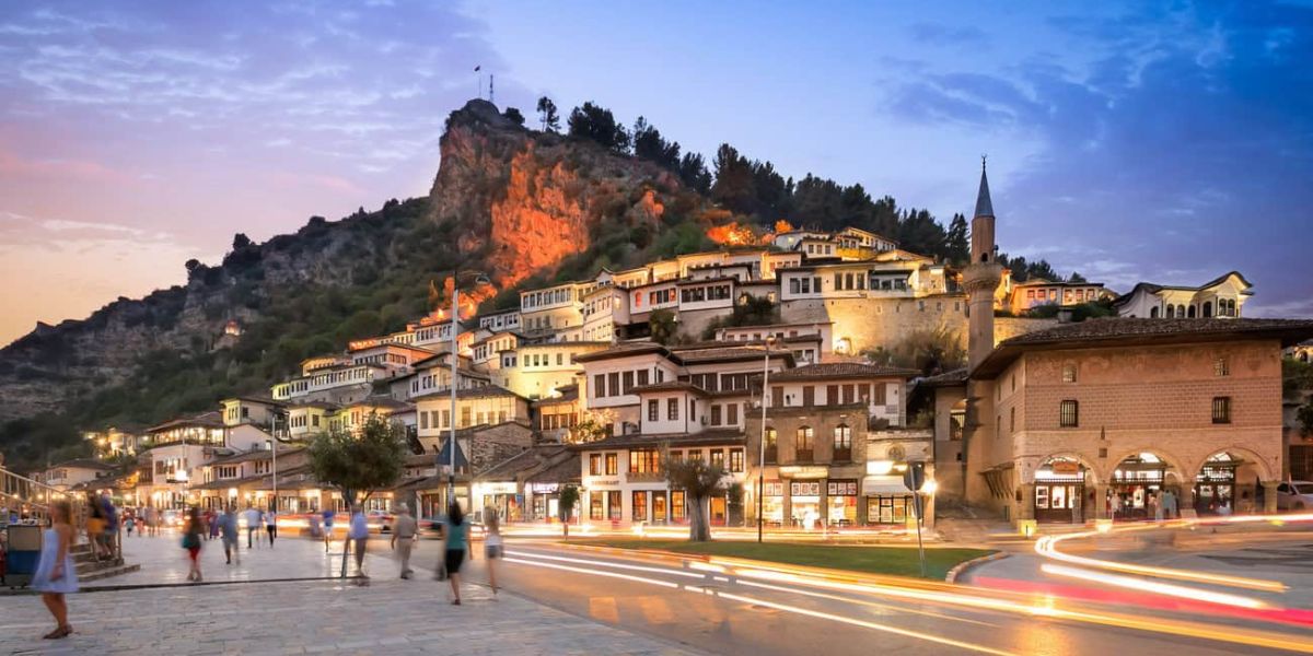 View of Berat, a UNESCO World Heritage City in Albania, featuring Ottoman-era white houses and the illuminated Berat Castle at sunset.