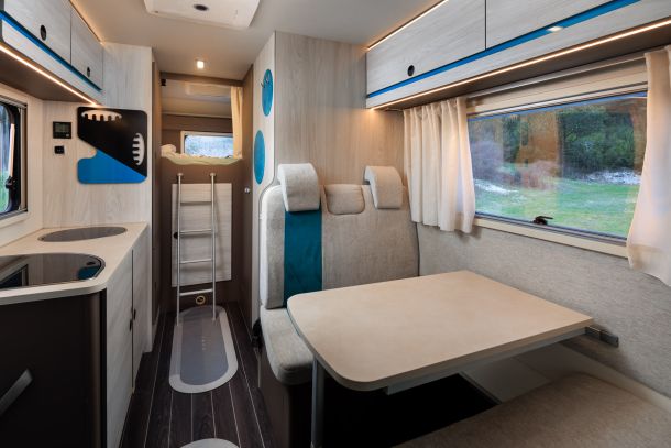 Inside a Nomad Camper in Albania, showcasing a cozy dinette with cushioned seating, a versatile table, and a view of the outdoors through a large window